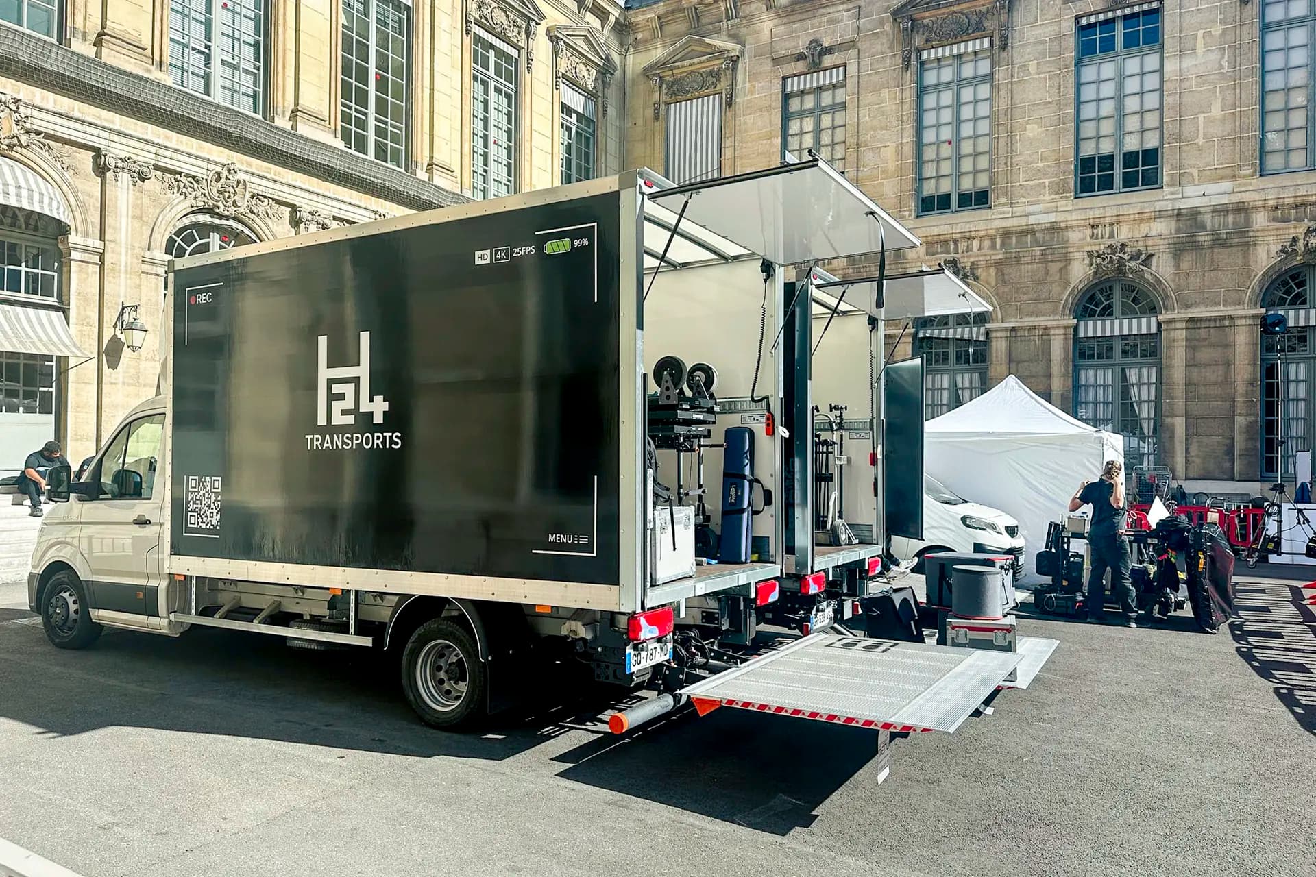 Camion H24 Transports hayon déployé sur un tournage, chargé de matériel de machinerie et de lumière