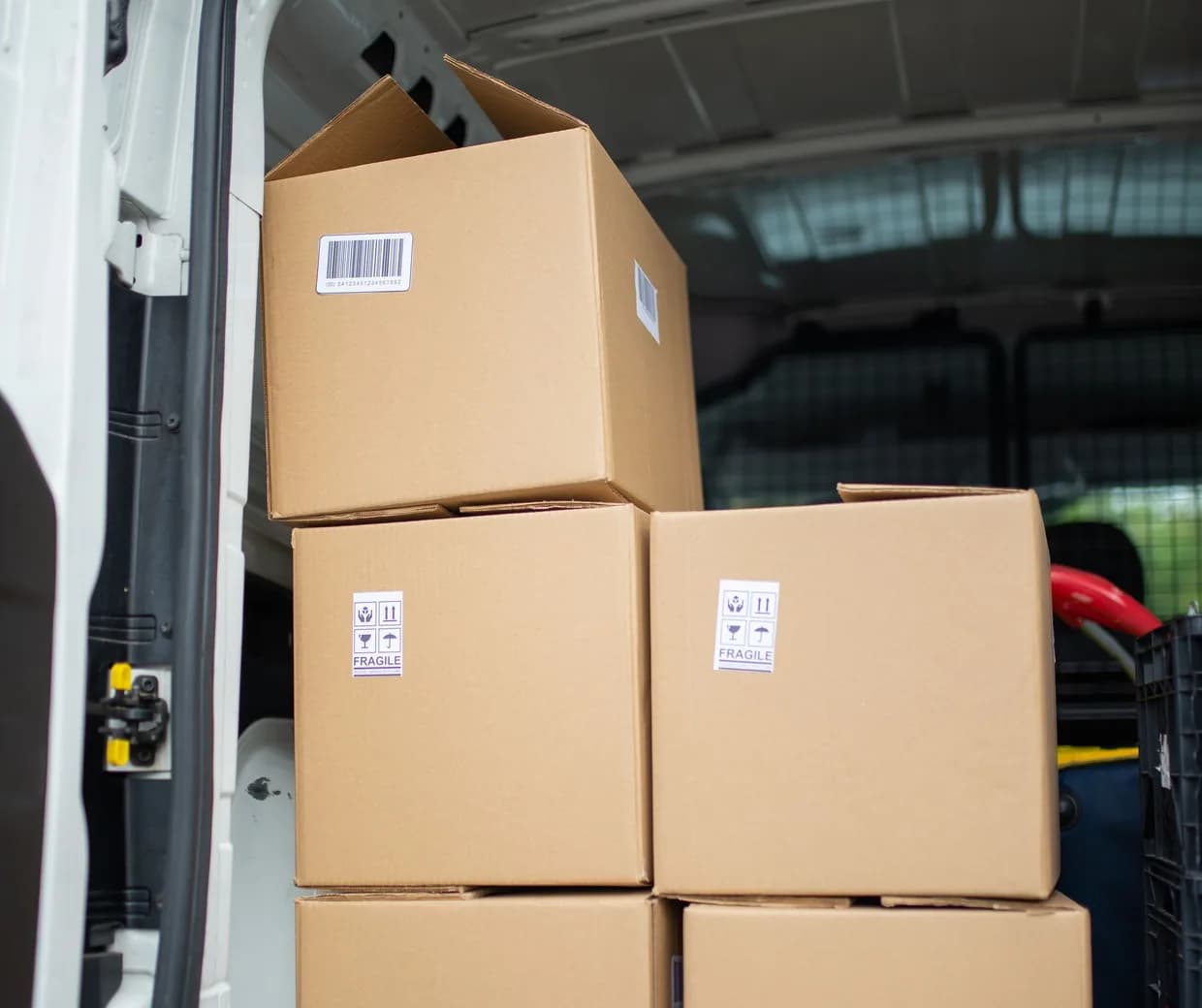 Cartons empilés dans un utilitaire blanc, porte arrière ouverte, étiquettes fragile