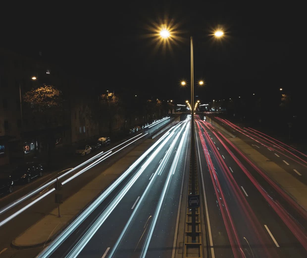 Voie rapide urbaine la nuit en pose longue, traînées de phares blanches et rouges sous les lampadaires